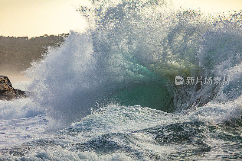 强大的风暴产生的海浪在海岸线上爆炸，在早晨的阳光下形成轮廓