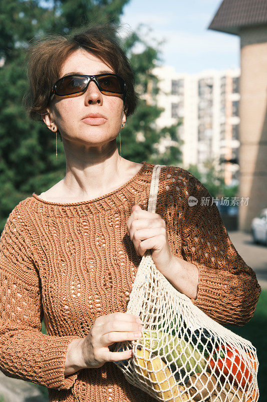 成熟的女人从超市回来，把商店装在可重复使用的购物袋里