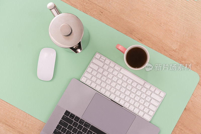 在笔记本电脑上的一杯咖啡的俯视图照片，白色鼠标在一个大的绿色垫木桌。网上。最小的。键盘。组织。遥远。工作。无线。规划。沟通。研究
