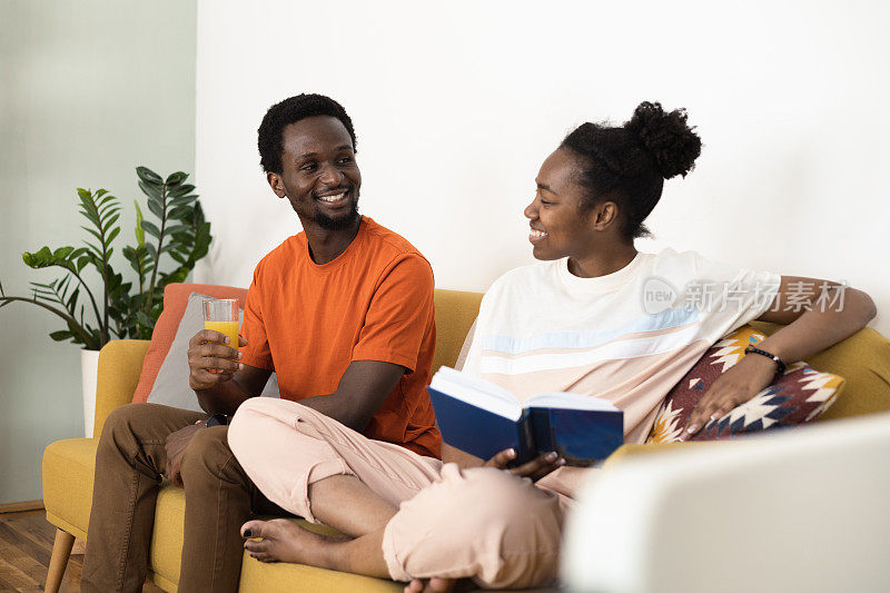 一对幸福的非洲夫妇的肖像享受在沙发上，谈论这本书