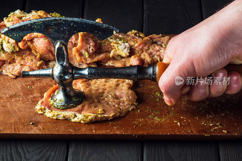 厨师用嫩肉剂把生小牛肉打烂。特写的工作环境和厨师的手在厨房的桌子上