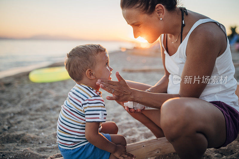 母亲在沙滩上给小儿子的脸上涂防晒霜