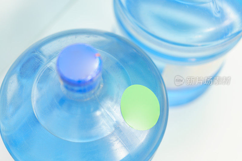两个塑料加仑水瓶容器的顶部，绿色圆形标签站在蓝色背景。健康。对象。透明的。明确的。瓶装。冷却器。新鲜。矿物