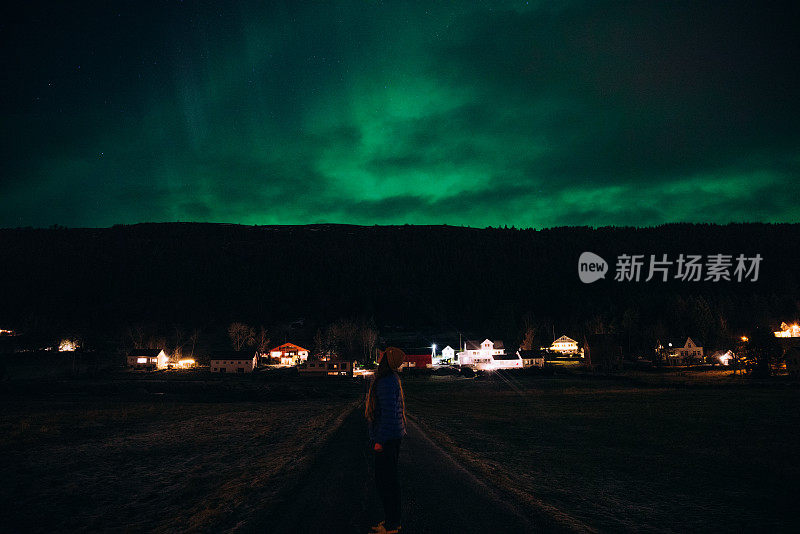 在挪威农村地区，一名女子在天空中欣赏强烈的北极光