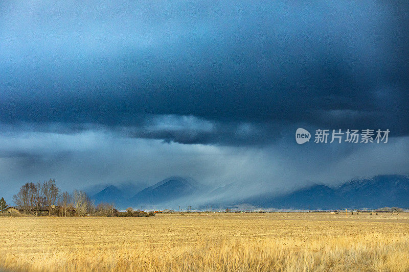 戏剧性的风暴云和雨在平坦的农田和雪山上移动