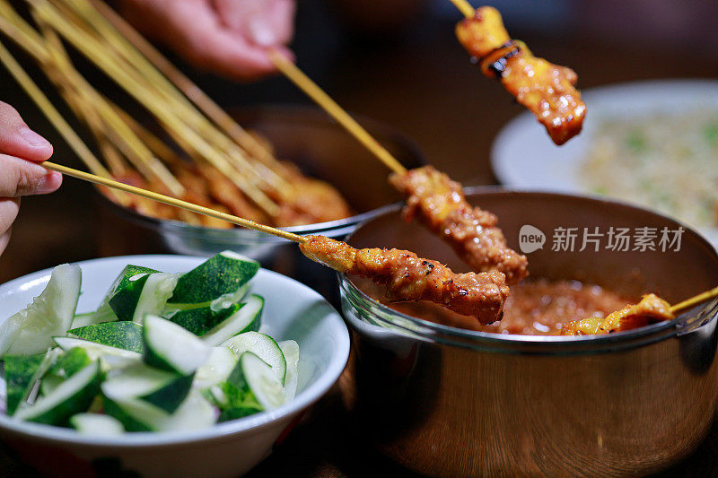 马来西亚美食，沙爹。在一张特写照片中，游客们正在品尝令人垂涎的马来西亚美食沙爹。沙茶与辛辣的花生酱搭配，创造出诱人的口味组合。