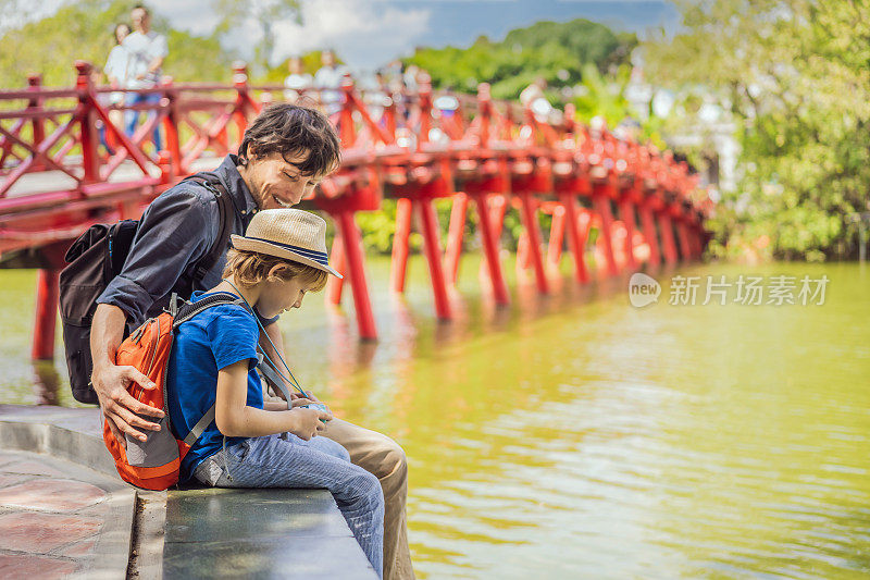 在河内市中心还剑湖中央的公园里，白人爸爸和儿子以红桥为背景，公园里有树和倒影。带孩子旅行概念