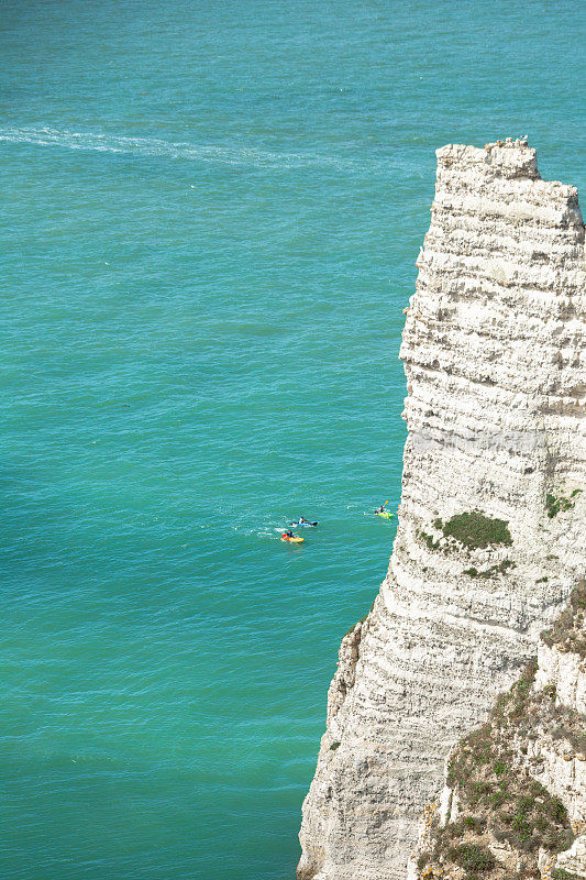 白色高耸的海崖从宝蓝色的大海中脱颖而出，人们在Étretat玩香蕉船