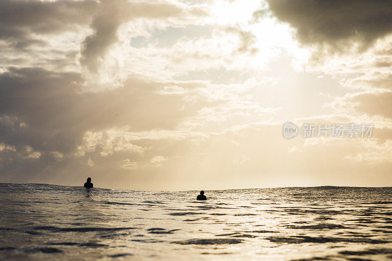 人在冲浪板上与日出和戏剧性的光线反射在海洋表面在金色的光