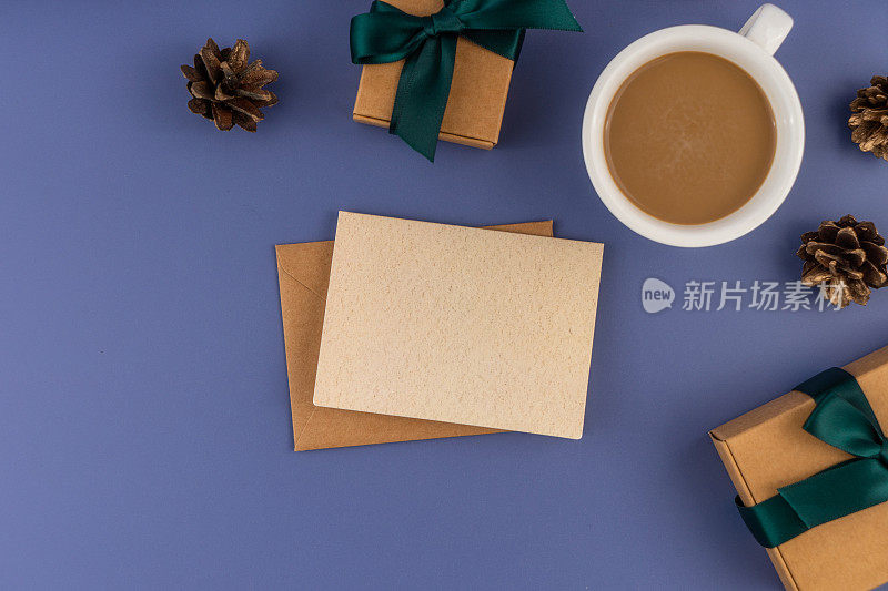 圣诞信件信封与空白纸卡，一杯咖啡和圣诞装饰在柔和的蓝色背景。
