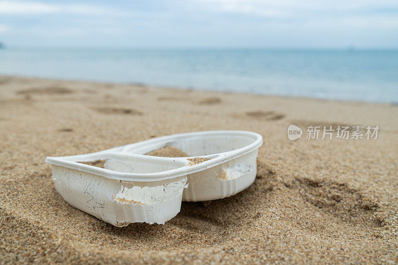 海滩上的白色塑料容器在阳光下的特写镜头，背景是大海，要求采取立法行动保护环境。