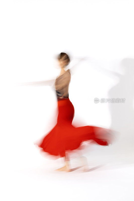 穿着红裙子的年轻芭蕾舞女演员在舞蹈室的灯光下跳舞。长时间的曝光。白色背景