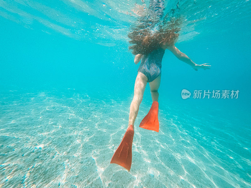穿着红色脚蹼的女孩在她的暑假里在水下游泳
