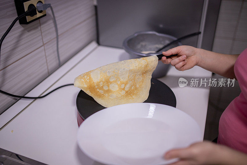 女人用锅铲在电煎锅上翻转煎饼