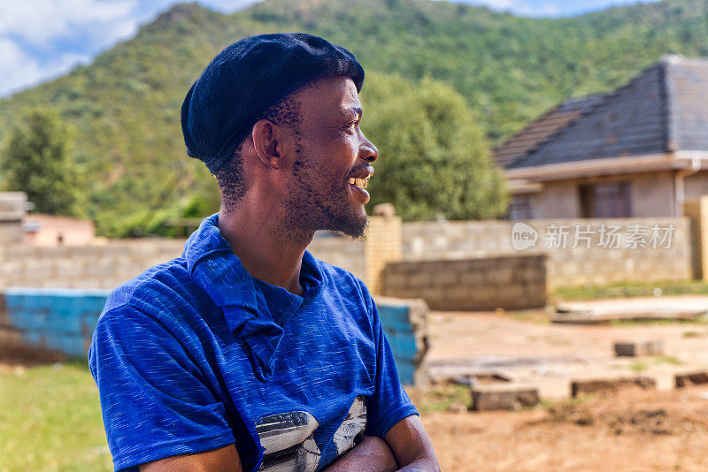 村子里年轻的非洲男子站在屋前的院子里，侧面看，