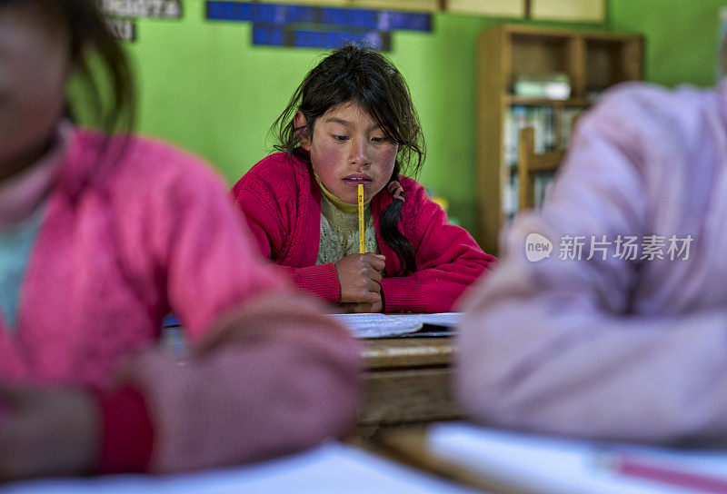 一名来自奎罗族的克丘亚女孩在学校上课，她的脸上带着沉思，嘴里叼着一支铅笔