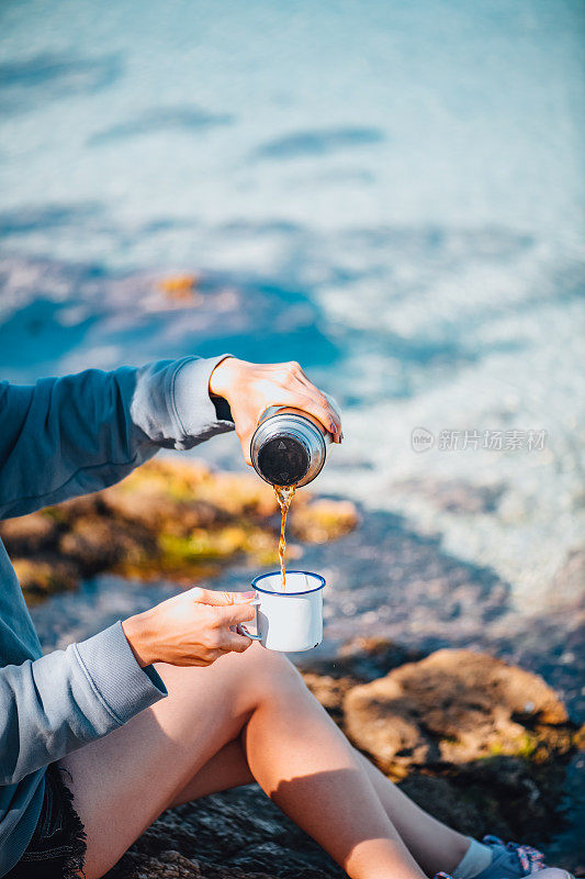 海滩上的女人从保温瓶里喝咖啡