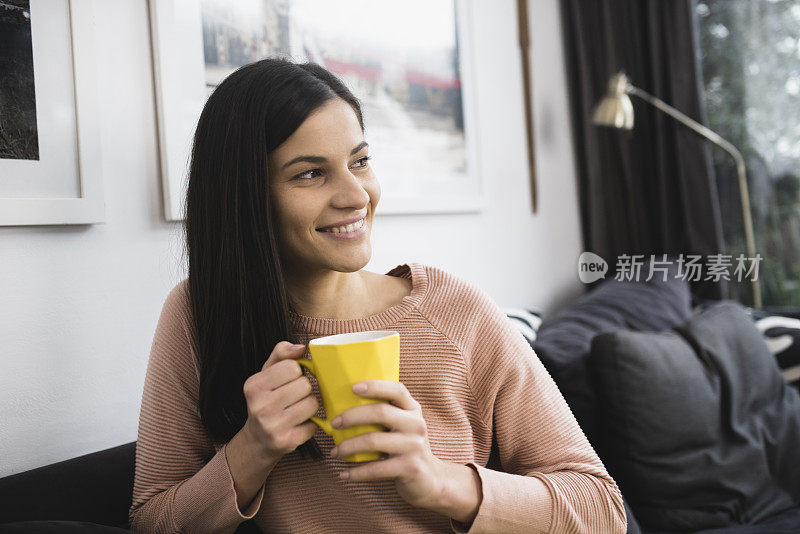 一个美丽的年轻女人享受咖啡和放松在家里的肖像