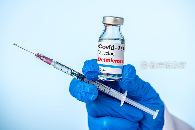 医生或护士用蓝色手套拿着Covid-19德尔米克隆变种疫苗和注射器。