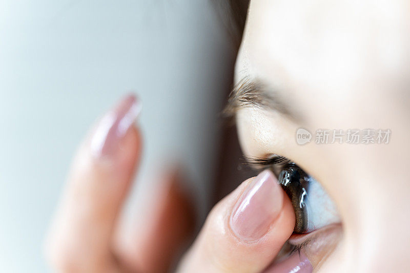 一名年轻的亚洲妇女将一枚棕色隐形眼镜戴在手指上。