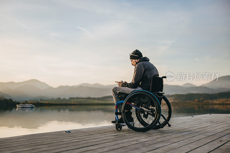 坐在轮椅上的残疾人在湖边的码头上使用智能手机