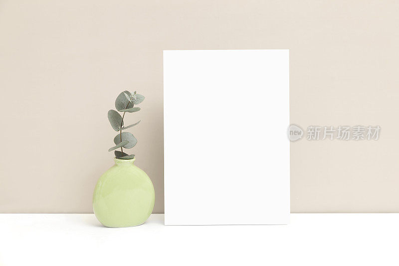 婚礼邀请或贺卡模型，一个花瓶和一根桉树小枝在米色的背景上。