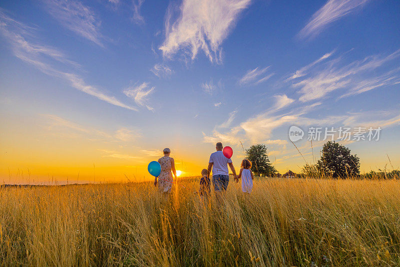 夕阳西下，一家人带着气球在草地上散步