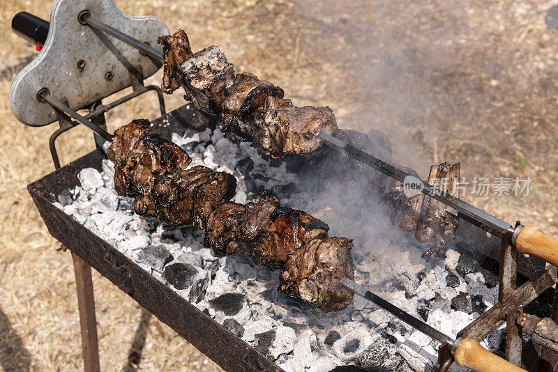 木制的旋转烤肉串与羊肉烹饪，白色的烟从覆盖着灰烬的木炭在露天烧烤