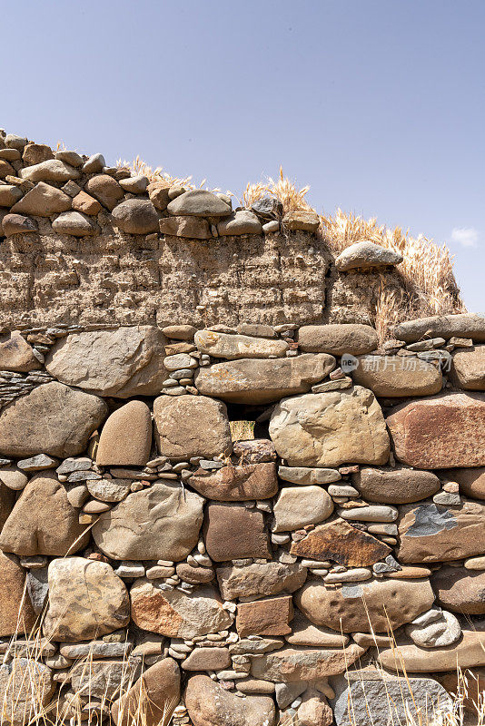 由多种天然岩石类型组成的石墙，上面是泥砖层，顶部是较小的岩石倾斜排列