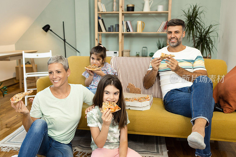 周末，幸福的年轻家庭吃着披萨，看着电视