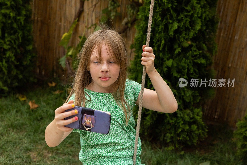 年轻的白人女孩坐在秋千上用手机自拍