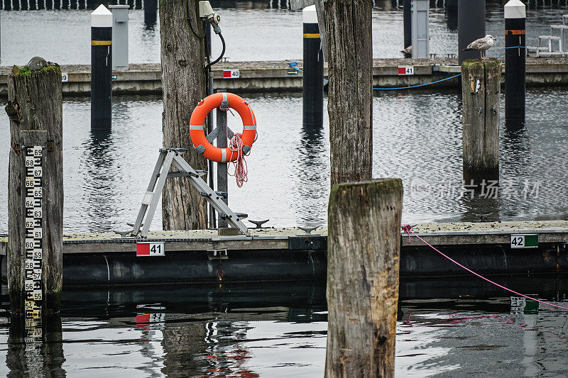 橙色的救生圈或救生圈挂在风化的木系泊桩上，或在波罗的海空游艇码头上的海豚，在一个灰色的11月的日子里，航海季节结束了，复制空间