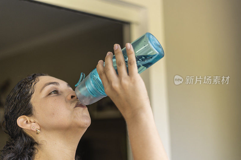 一名拉丁妇女用绿色瓶子喝水