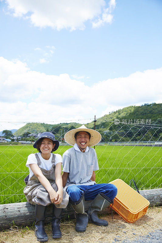 一男一女微笑着坐在稻田前的圆木上