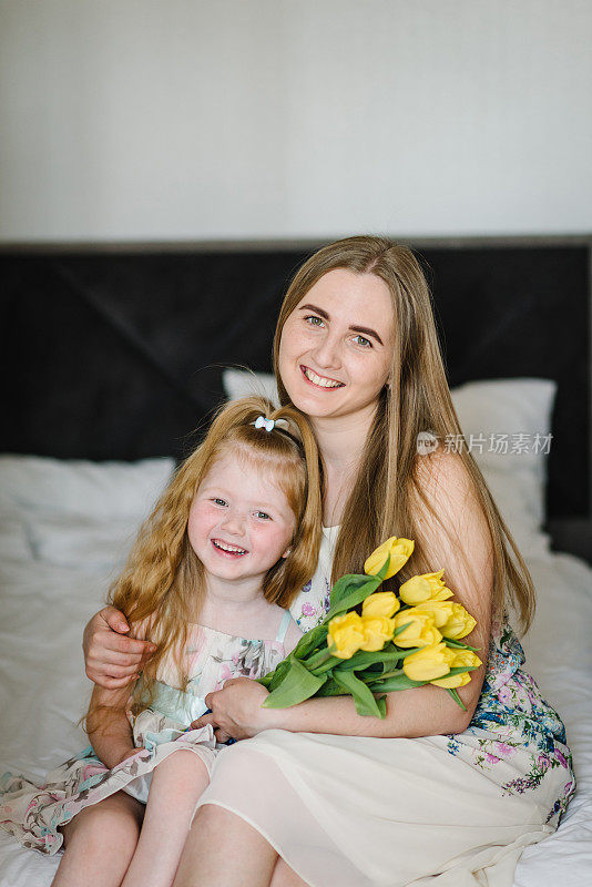 母亲节的概念。女孩向母亲表示祝贺，并在家里送了一束黄色的郁金香。妈妈和女儿微笑着拥抱。国际妇女节的节日贺卡。特写镜头