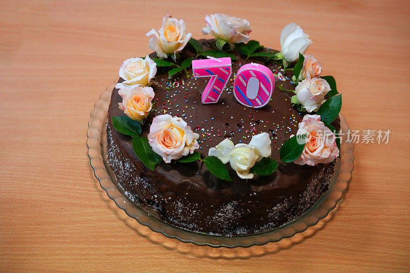 为70岁高龄生日准备的巧克力蛋糕，配上新鲜的玫瑰，配上餐桌背景。
