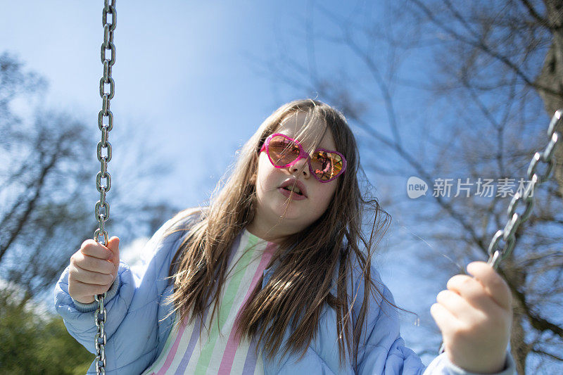 戴粉红色眼镜的年轻女孩在秋千上