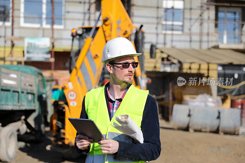 男建筑师在工地使用数码平板电脑，他穿着防护背心和头盔