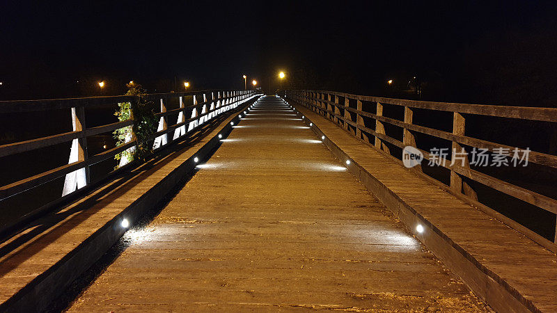 巨大的破旧的木桥，木扶手在晚上更新了装饰性的现代LED灯
