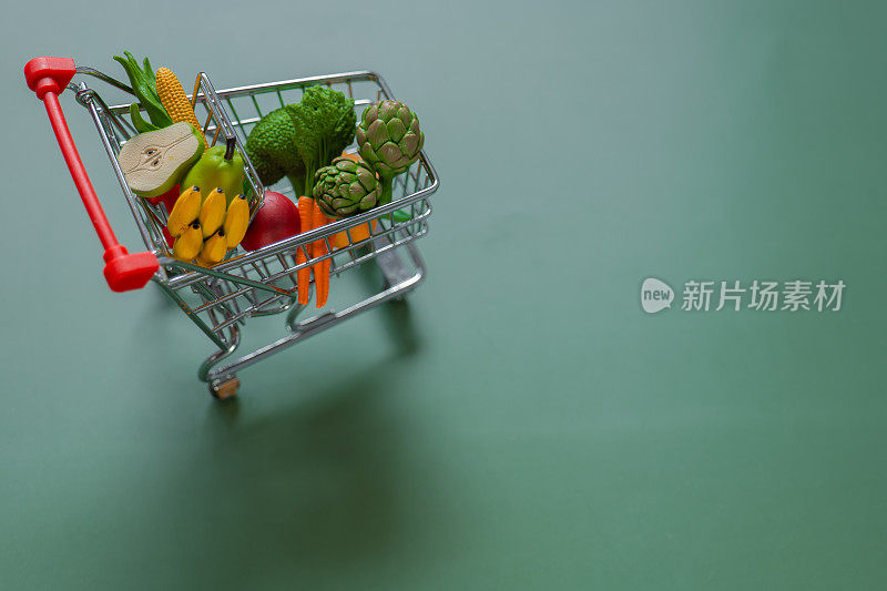 绿色背景上有杂货的购物车。蔬菜和水果价格。装饰超市手推车与杂货。食品价格。
