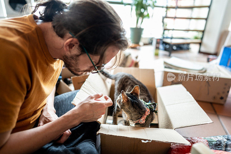 中年男子和他的宠物猫在家里的盒子里开玩笑