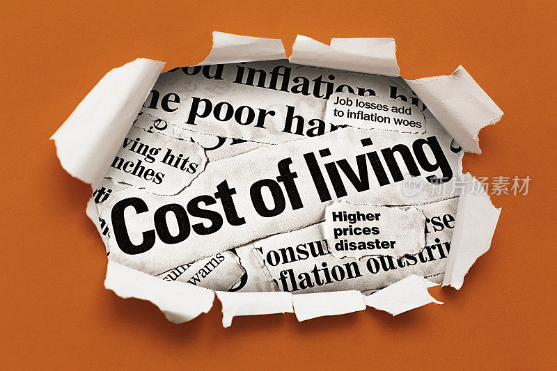 报纸上关于生活成本和通货膨胀的大标题，从边缘撕成锯齿状的纸洞里透出