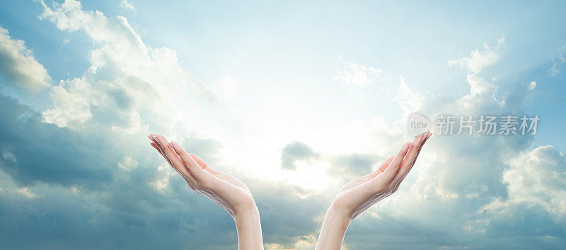 两只张开的女性的手映着白云和阳光的蓝天