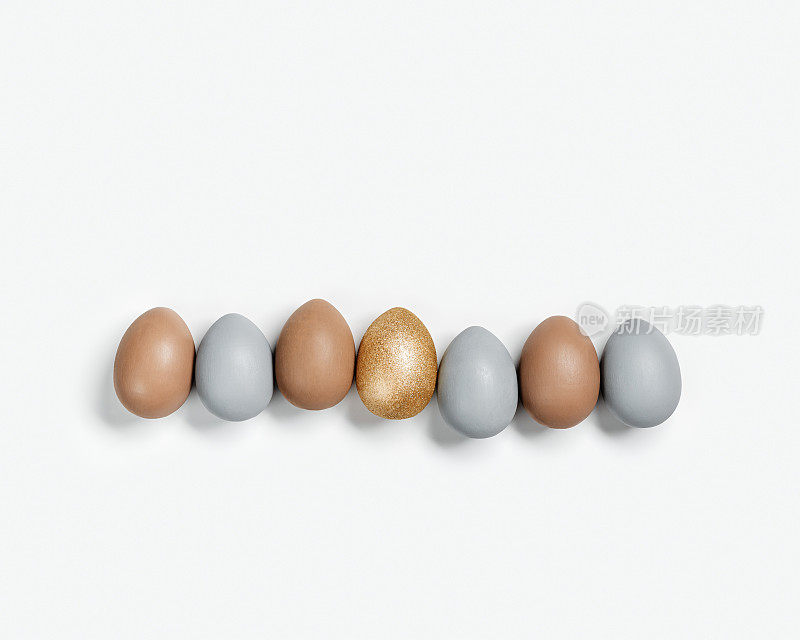 染色的复活节彩蛋柔和的颜色灰色，米色和金色在白色的背景排。快乐复活节假期，庆祝美食理念，鸡蛋中性新潮色彩。顶视图表