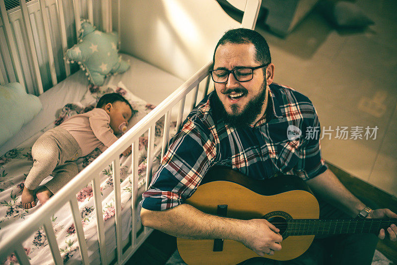 一位年轻的父亲一边弹吉他一边唱歌哄孩子入睡