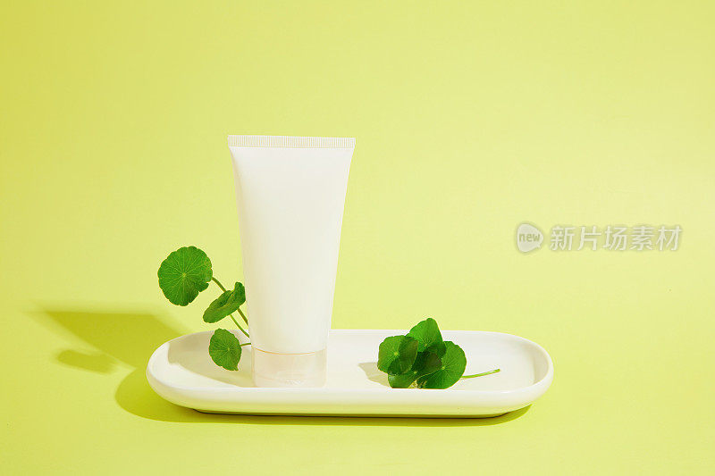 新鲜的草叶和一管洗面奶陈列在一个白色的陶瓷托盘上。精美的纯素化妆品广告背景。