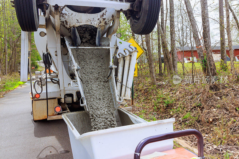 在一个建筑工地，湿水泥从水泥卡车的滑道上下来，进入一辆手推车轨道混凝土小车