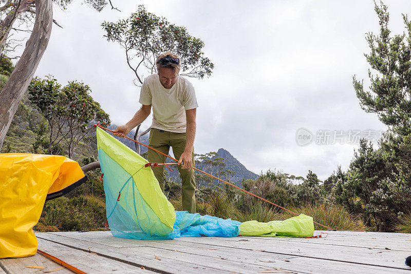 荒野静修:在塔斯马尼亚宁静的风景中，一名男子在木平台上搭帐篷