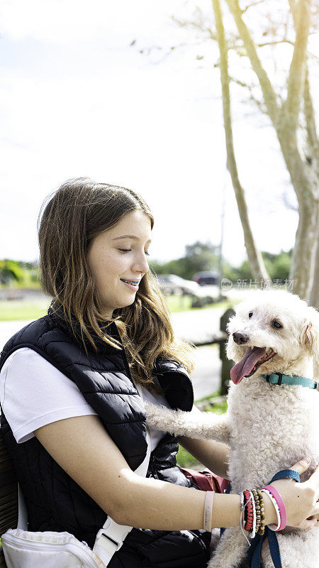 一个十几岁的女孩在公园的长椅上等公交车，带着宠物狗在附近的户外