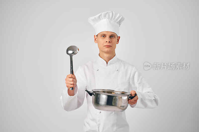 一个穿着厨师制服的男人，手里拿着平底锅和长柄勺在准备食物